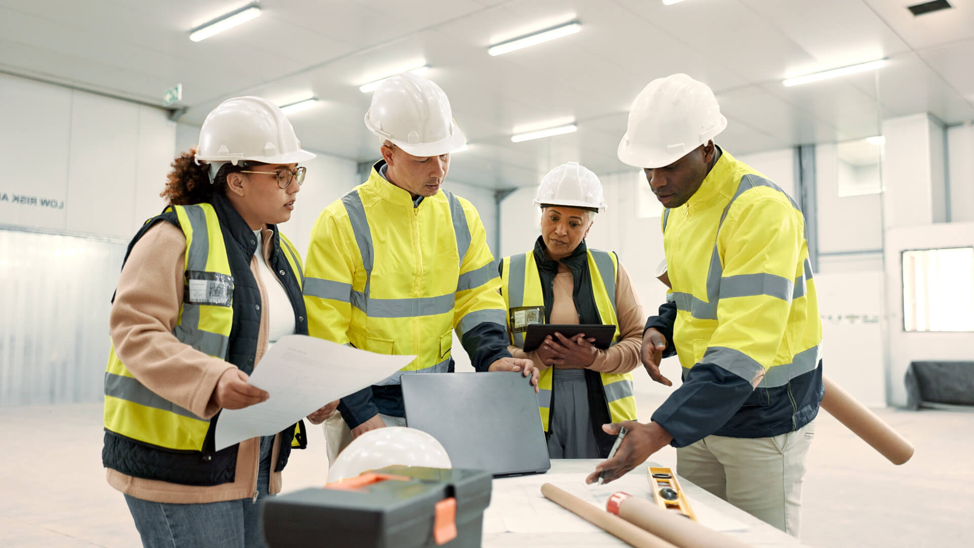 Four construction workers gathered around blueprints and tools displaying a strong workplace safety culture.