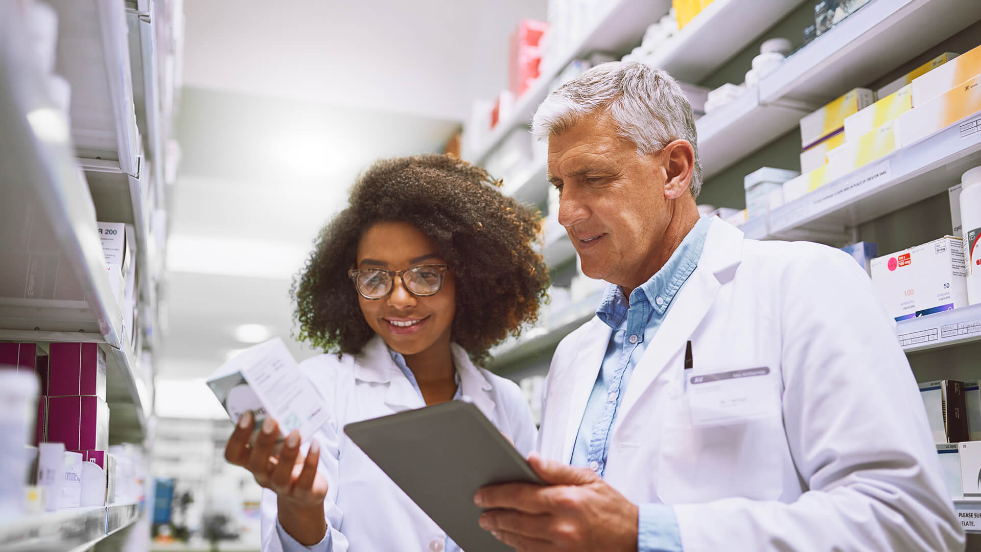 Female and male pharmacists filling orders while discussing the future of pharmacy workforce shortages and industry shifts.