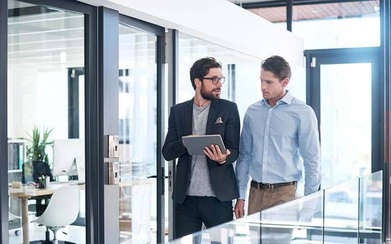 Two men walking through an office looking at tablet