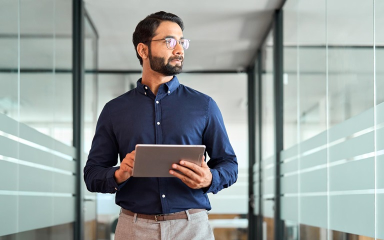 man gazing out the window holding a tablet