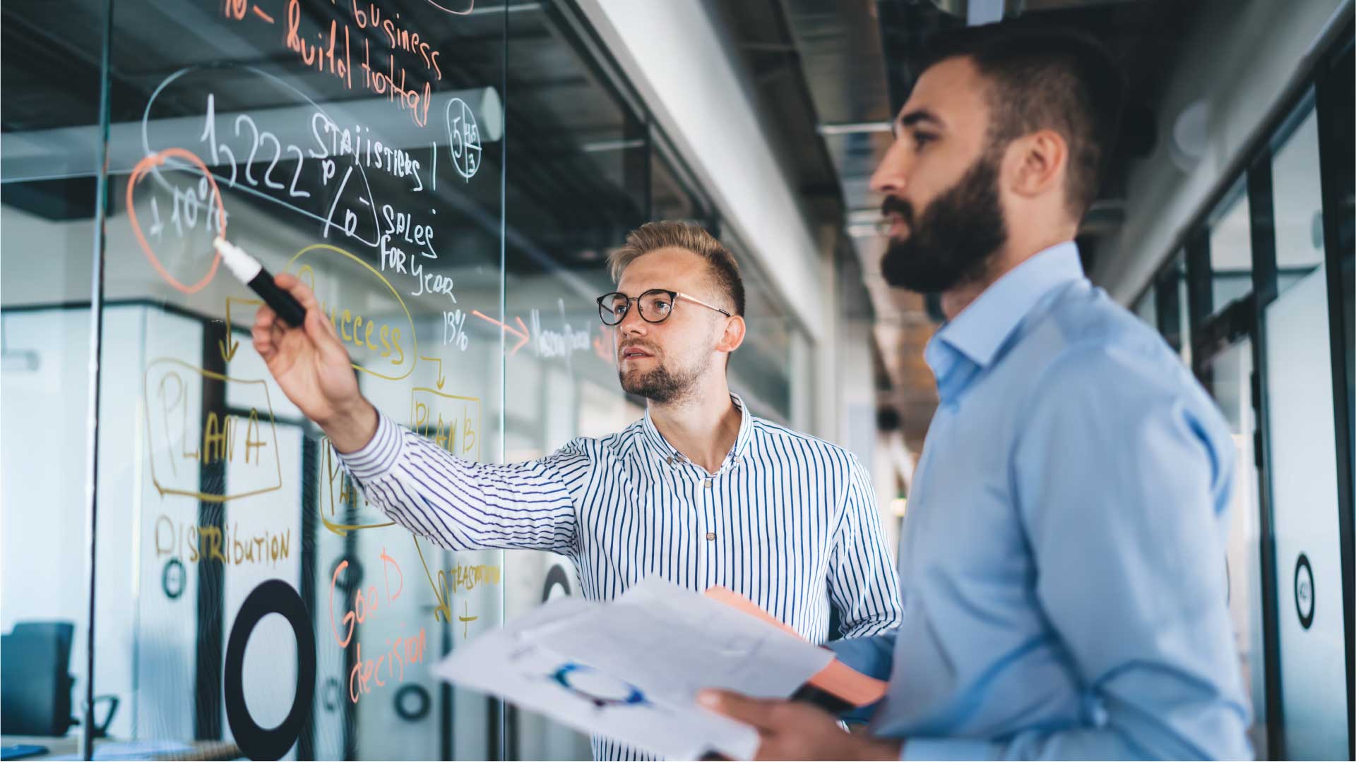 two male coworkers writing data on transparent wall