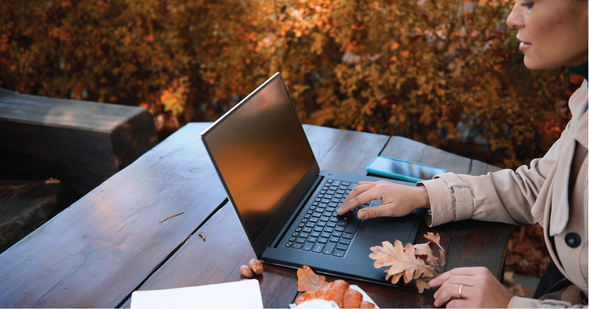 woman on her laptop sitting at a picnic table outside during Fall