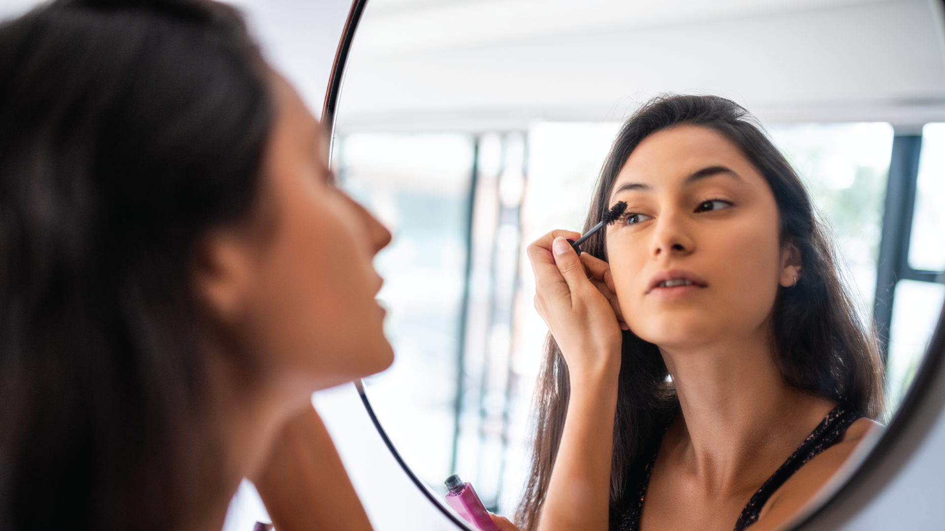 young woman looking into mirror putting on mascara