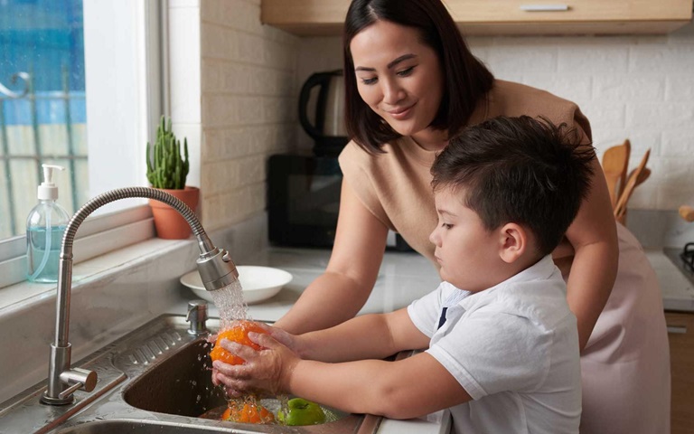 little boy rinsing fruit under tap water with his mother
