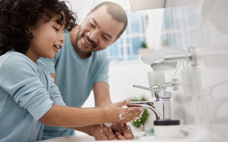 Father helping his child wash his hands and face at a tap in a bathroom at home